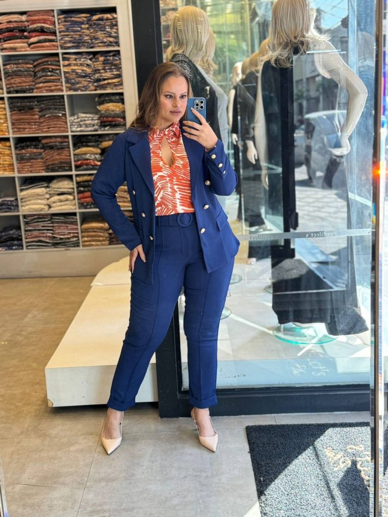 Modelo mulher usando calça e blazer no tom azul marinho, blusa por baixo no tom laranjado com detalhes em branco