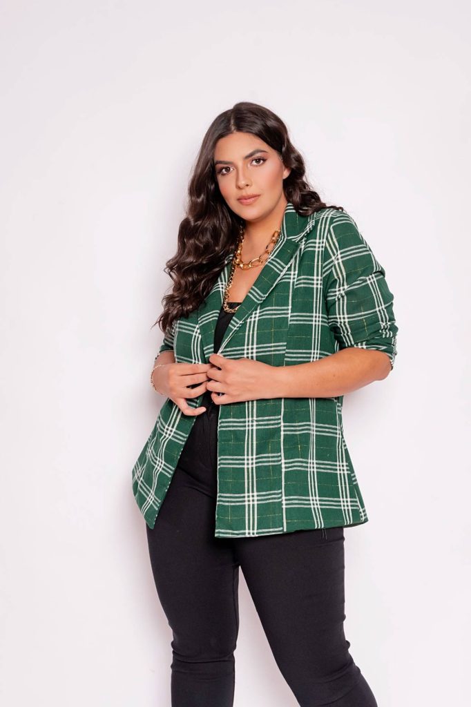 Mulher modelo usando blazer verde com detalhe em xadrez na cor branca, blusa e calça preta